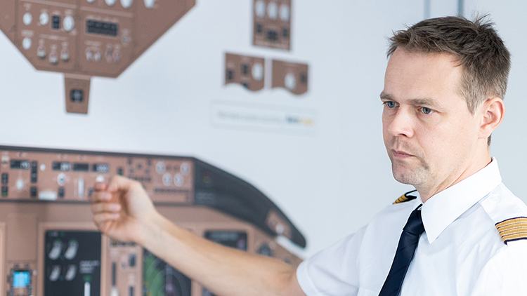 A pilot stands in front of a board showing an aircraft cockpit