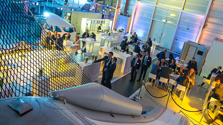 In a colourfully illuminated training centre there are bar tables and stools between the training equipment and around 30 guests