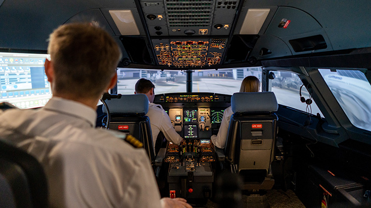 View into a cockpit simulator with two pilots and an instructor