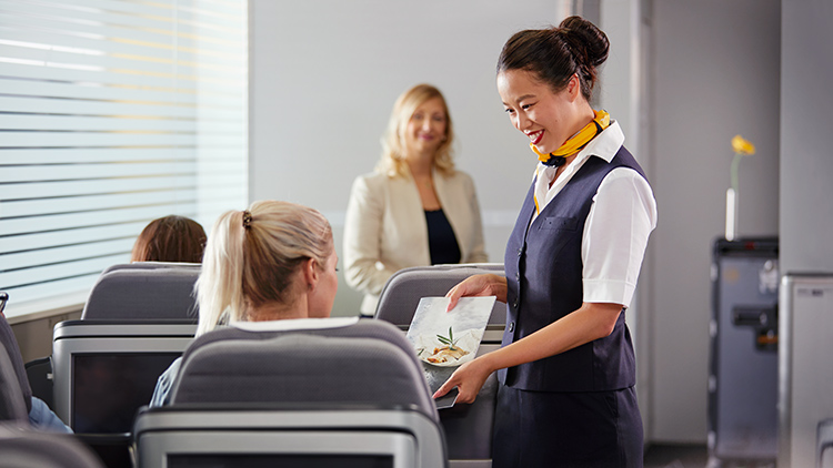 A flight attendant offers the menu to a passenger in a training situation.