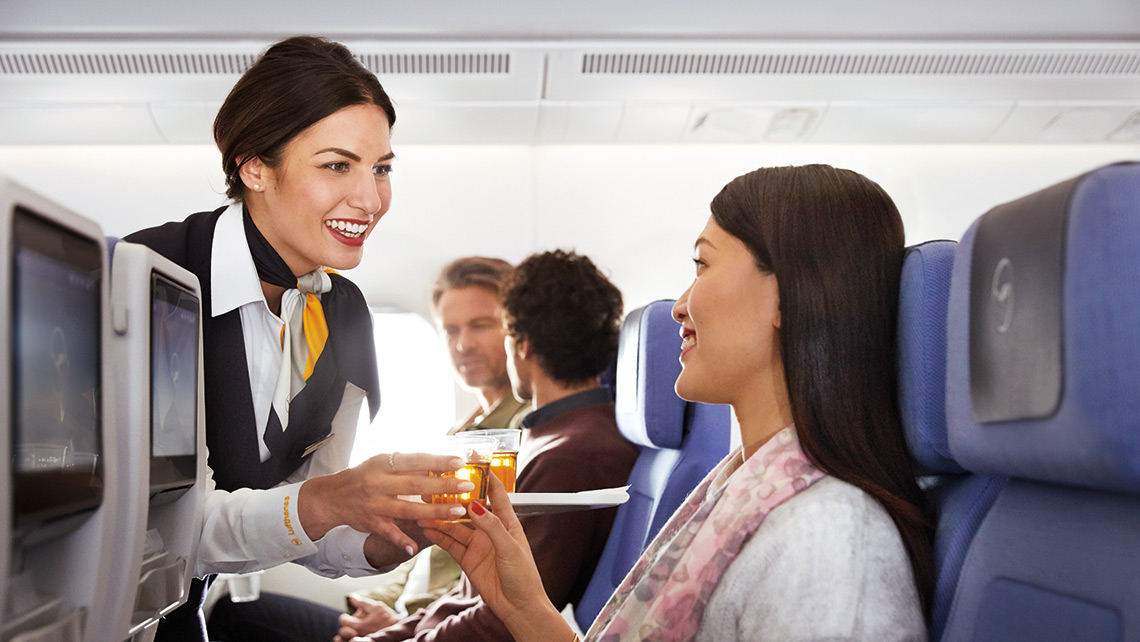 A flight attendant serves a passenger a drink during the flight