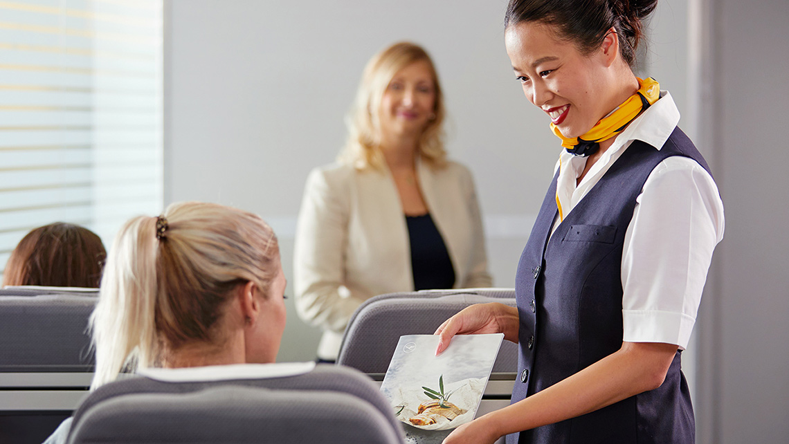 A flight attendant offers the menu to a passenger in a training situation.