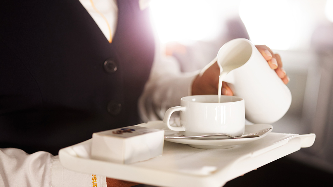 Close-up of a tray in the hands of a flight attendant pouring milk into a cup of coffee