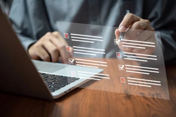 A person sits at a laptop, a checklist is displayed in front of them.