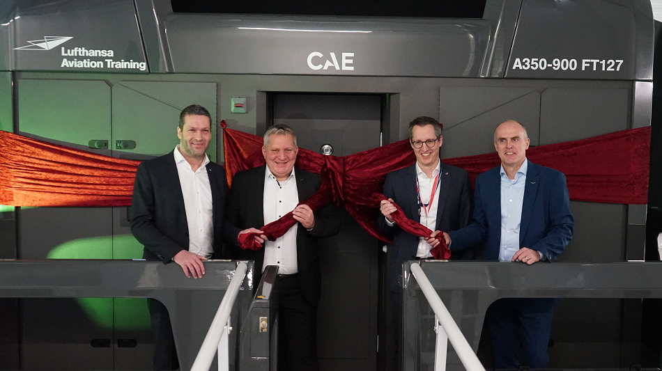 Four people are standing in front of a flight simulator wrapped with a ribbon.