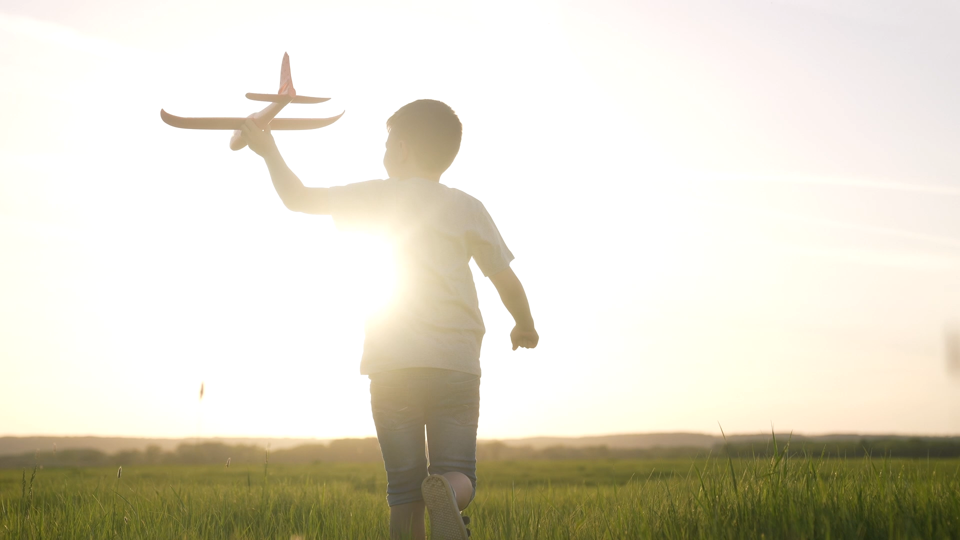 A child with a model airplane in hand is running across a meadow.